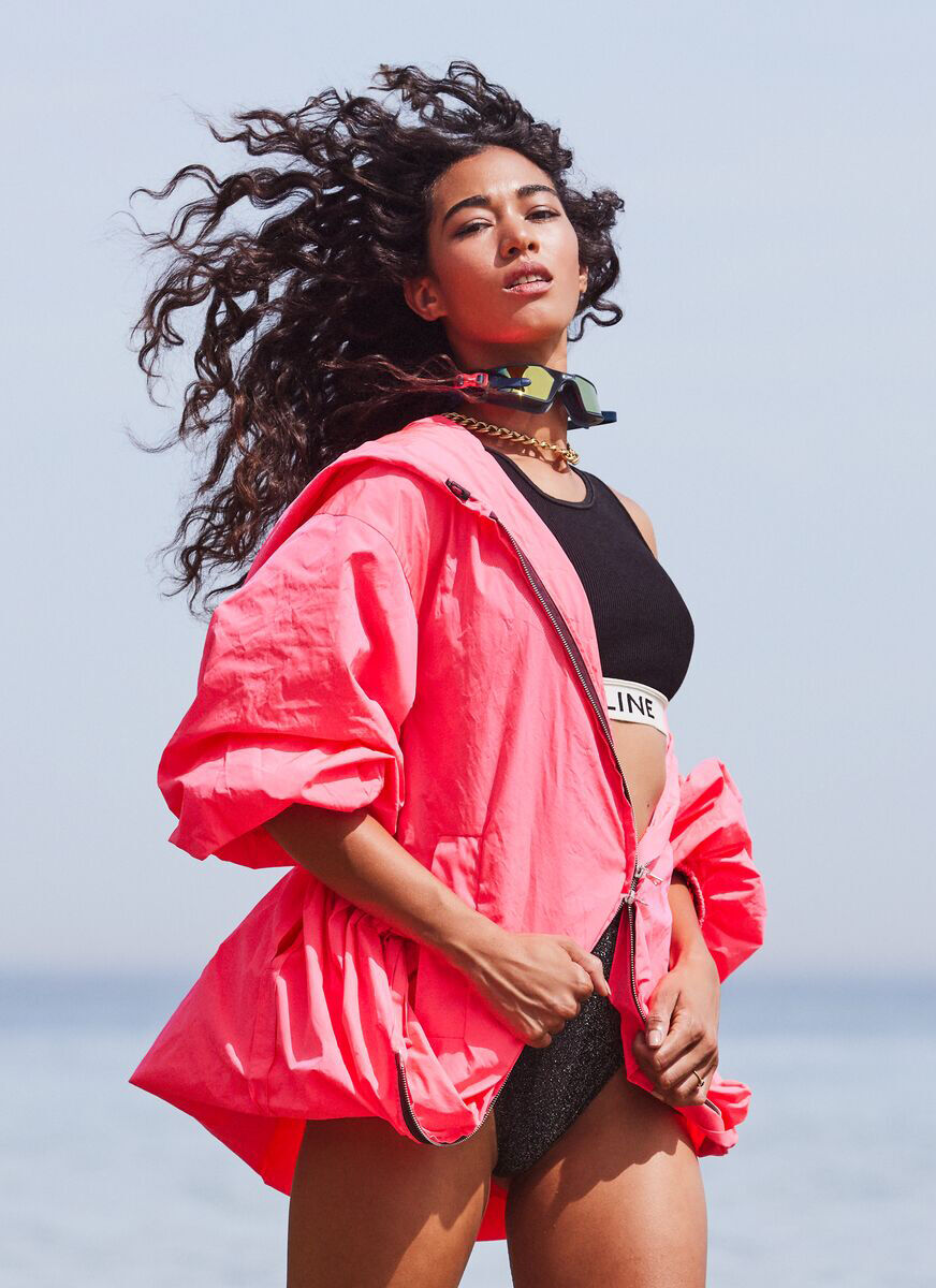 Young woman with free-flowing natural hair texture standing against a coastal backdrop.
